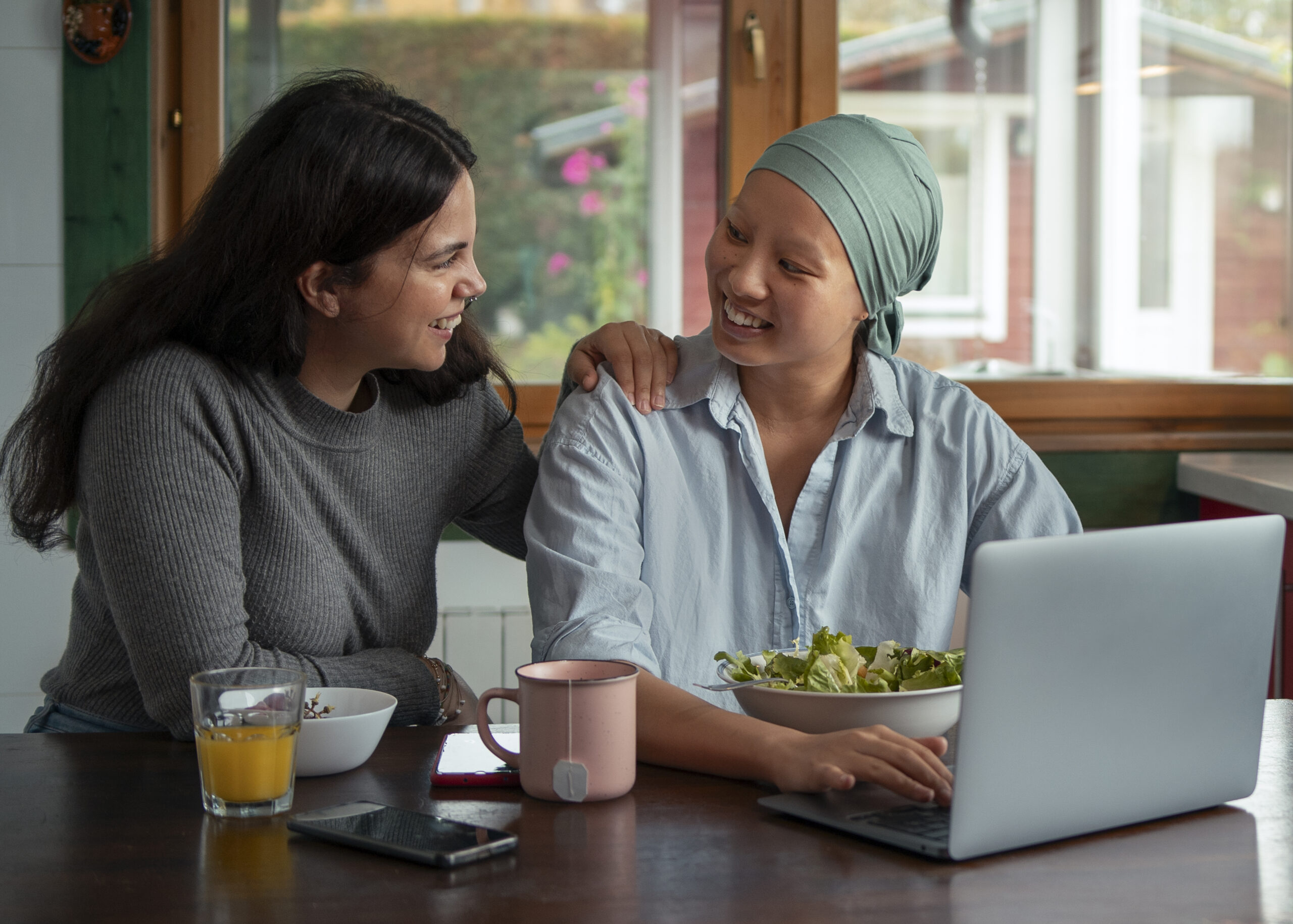 portrait woman with cancer using laptop with friend home